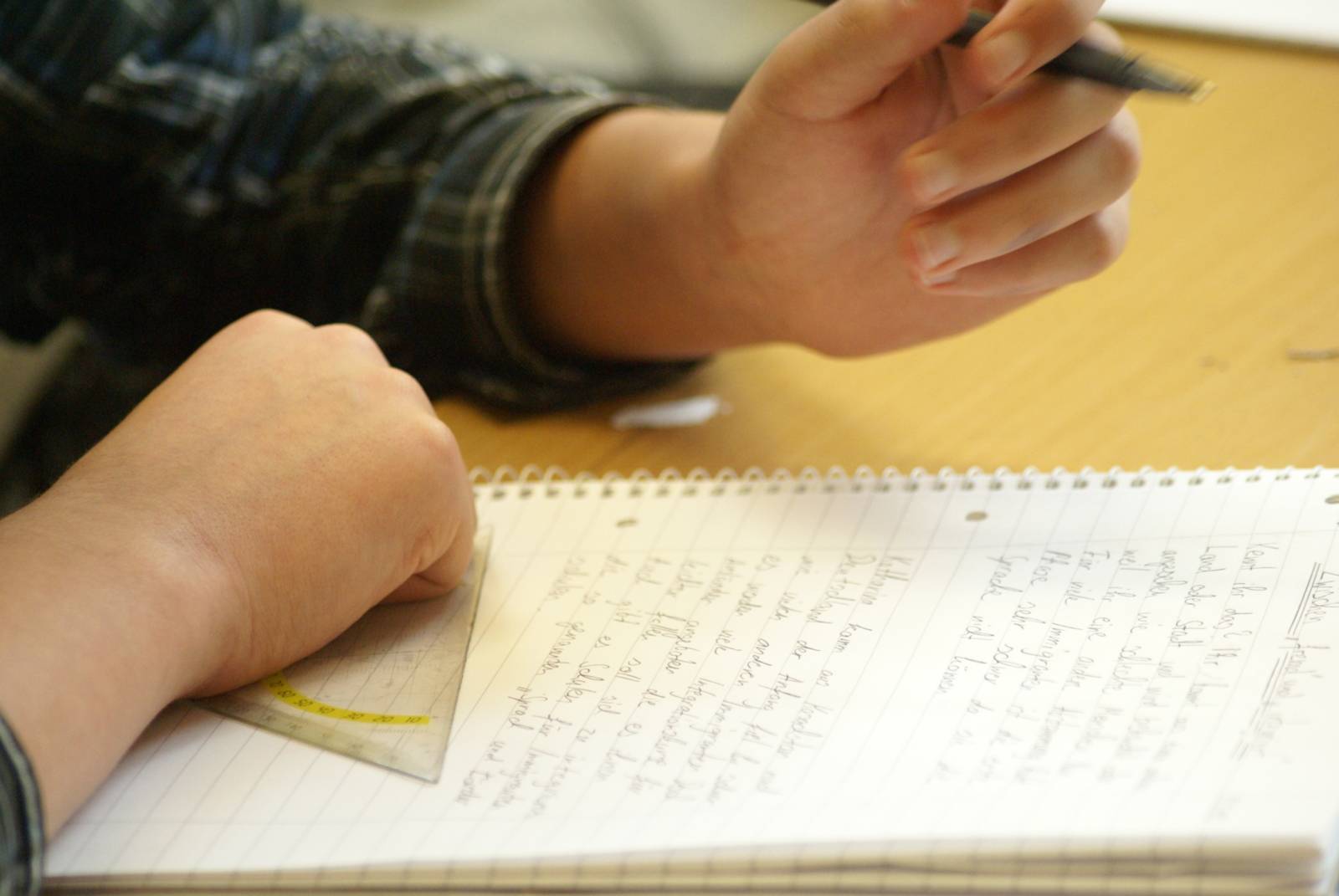 Ein Kind schreibt auf einem Collegeblock. Es hält einen Stift und ein Geodreieck in den Händen.